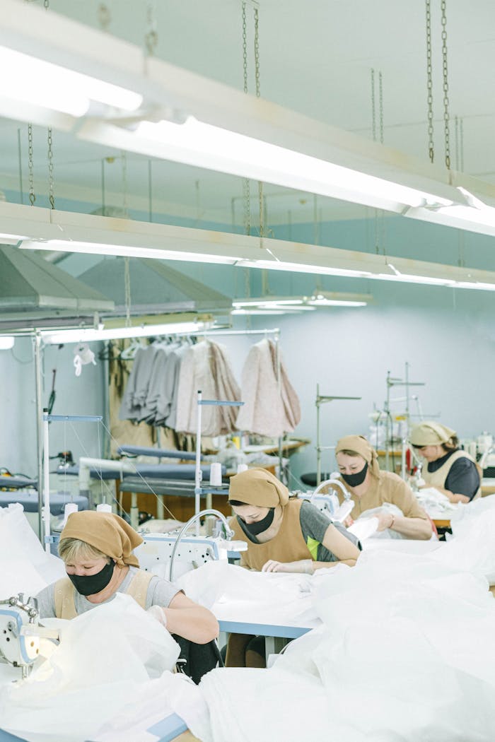 our-services-1 Women sewing with machines in a textile factory, wearing face masks and headscarves.