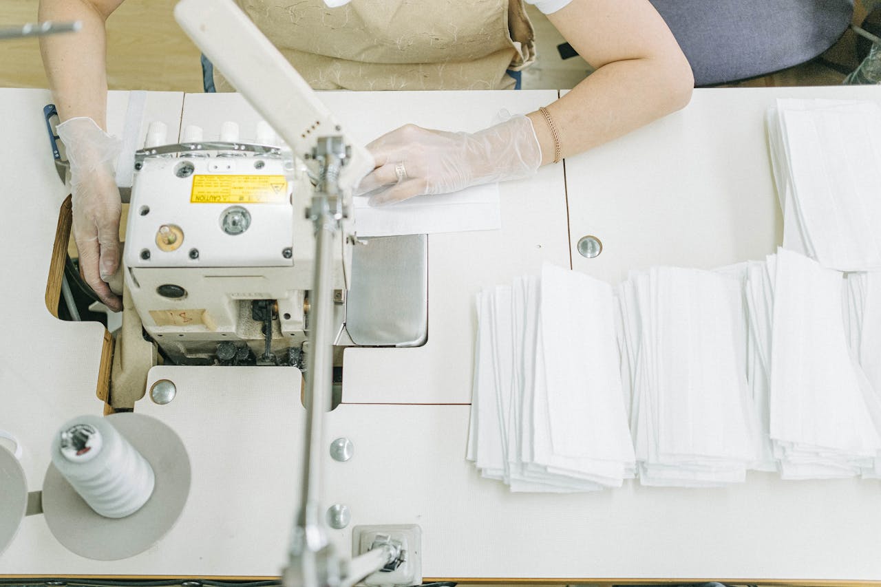 our-services-3 Overhead view of a person sewing white fabric using an industrial sewing machine indoors.